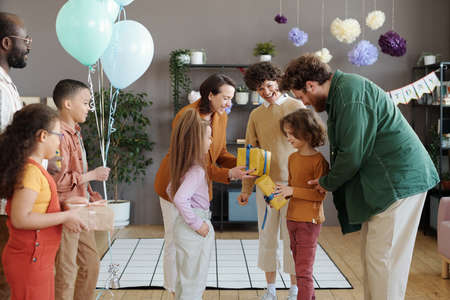 Little boy taking presents from his friends during birthday, they coming with parents for party to...