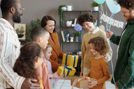 Parents and friends with kids congratulating boy with birthday giving him presents during home partyの写真素材