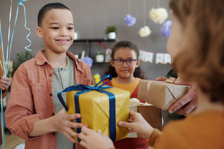 African little boy giving gift box to his friend and congratulating him with birthday during party at homeの写真素材