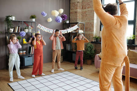 Group of children playing and dancing with animator in animal costume during birthday party at homeの写真素材