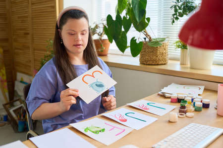 Young female in casualwear taking paper with letter E and picture of elephant painted by herself...