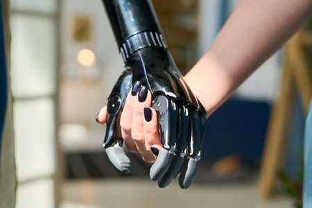 Young woman with black nail polish on her fingernails holding by myoelectric hand belonging to...