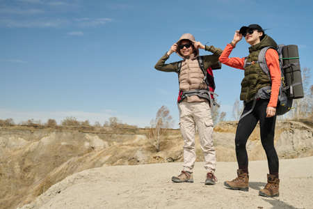 Horizontal long shot of two young Asian women wearing backpacks hiking in quarry on sunny spring dayの写真素材