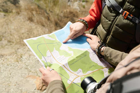 High angle of two unrecognizable women wearing backpacks hiking together on sunny spring day reading...