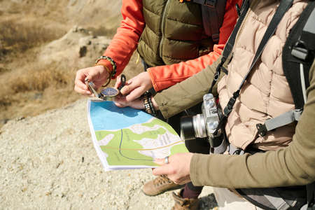 Unrecognizable female tourists wearing backpacks hiking together on sunny spring day reading paper...
