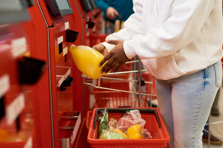 Female consumer in casualwear scanning chosen food products in self sesrvice terminal while buying...