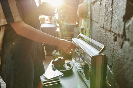 Close-up of girl in stylish casualwear choosing musical station while turning amplifier on portable radio receiver in the morningの写真素材
