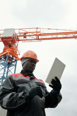 Modern experienced builder or foreman looking at screen of digital tablet during network or online...