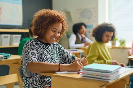Happy female teenager with pen making notes in copybook during lecture or individual assignment...