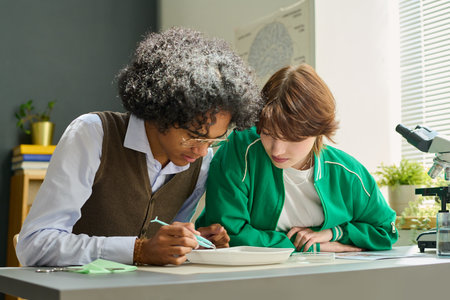 Two teenage intercultural students of highschool doing dissection of frog at lesson while one of...