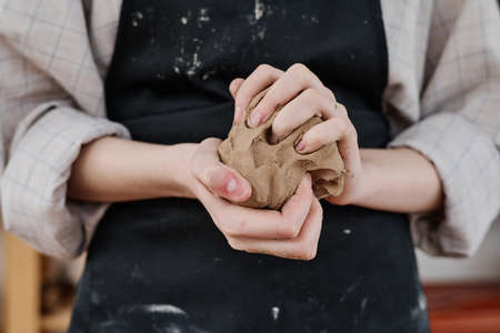 Hands of young creative woman in workwear holding piece of soft clay and kneading it while preparing for making earthenware productsの写真素材