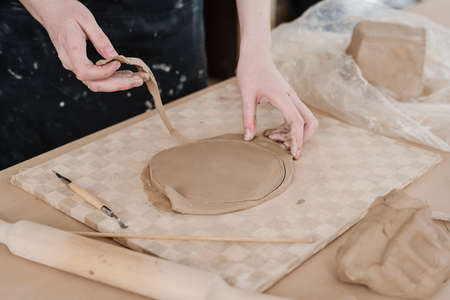 Hands of young craftswoman in apron taking away excessive clay to get accurate round shape of workpiece for creative eaarthenware itemの写真素材
