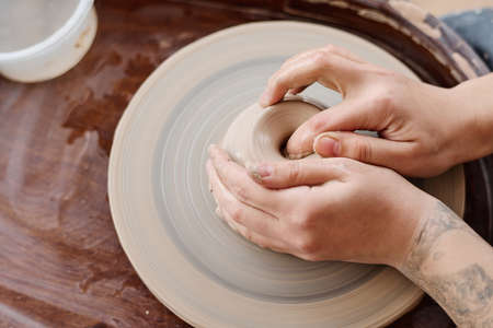 Above shot of hands of young creative female potter or owner of workshop sitting by pottery wheel and making clay productの写真素材