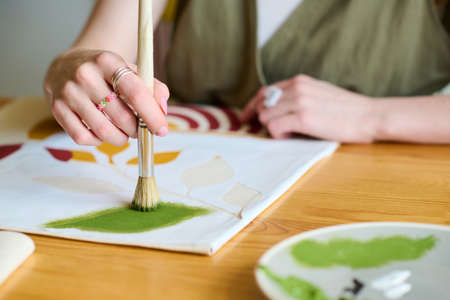 Hand of young creative female artist with paintbrush putting green watercolor on paper while creating new abstract paintingの写真素材