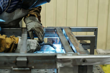 Gloved hands of male worker of industrial plant producing huge machines bending over workbench and...