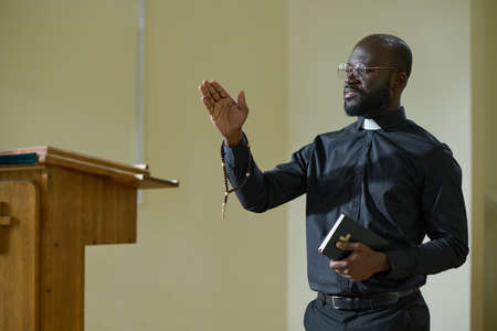 Confident African American man in pastor apparel with clerical collar preaching during church service in front of parishionersの写真素材