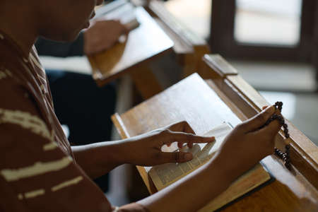 African American woman keeping finger on verse on page of Holy Bible while reading Gospel or one of...