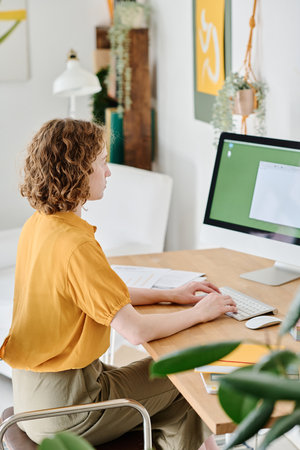 Young freelance webdesigner in casualwear with her hands over keyboard looking at electronic...