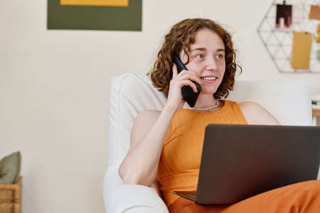 Happy young woman in smart casualwear ordering things in online shop by mobile phone while sitting...