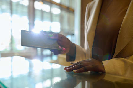 Hands of young black woman in smart casualwear passing her passport over counter to manager or...