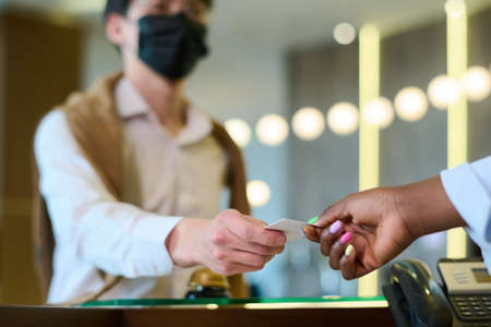 Hand of young black woman taking keycard held by male guest in casualawear and protective mask over...