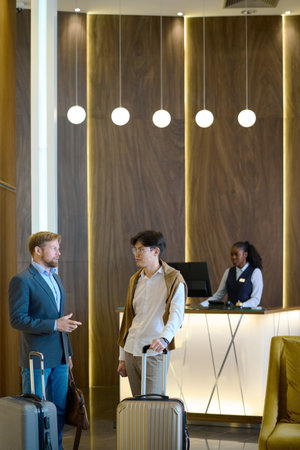 Two young elegant businessmen with baggage discussing working points of travel while standing by...