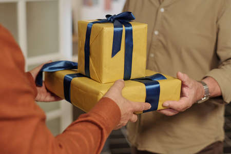 Hands of senior man passing giftbox wrapped into yellow paper with birthday present to his buddy during celebration of life eventの写真素材
