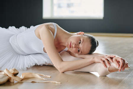 Graceful and flexible woman keeping her head on stretched leg while practicing choreographic...