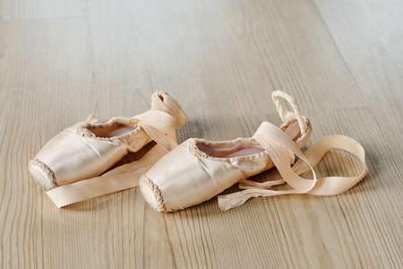 Pair of new untied pointe shoes of beige color with silk ribbons on the floor of dance hall or classroom for repetitions of ballet exercisesの写真素材