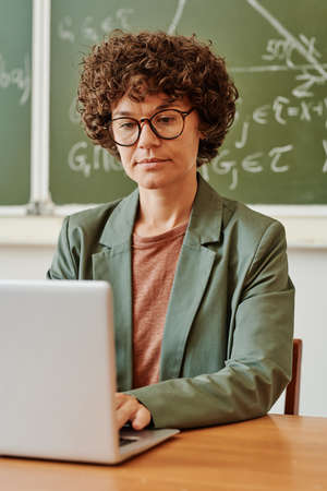 Young serious teacher concentrating on work with electronic documents or tables while typing on...