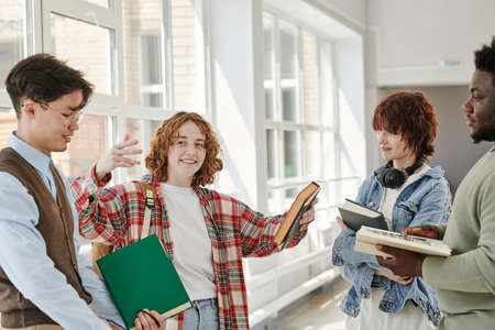 Happy teenage girl in casualwear explaining her intercultural classmates plot of the book during...