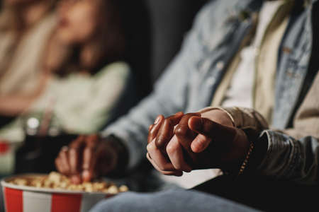 Selective focus of unrecognizable ethnically diverse couple holding hands while watching film at cinemaの写真素材