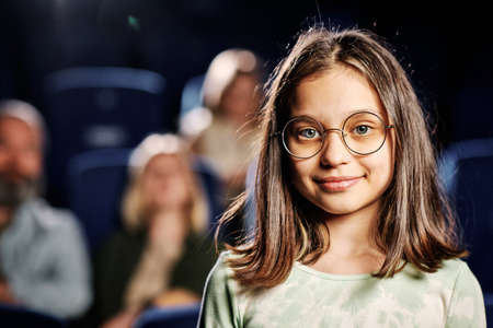 Portrait of preteen Caucasian girl wearing eyeglasses standing against seats at cinema looking at cameraの写真素材