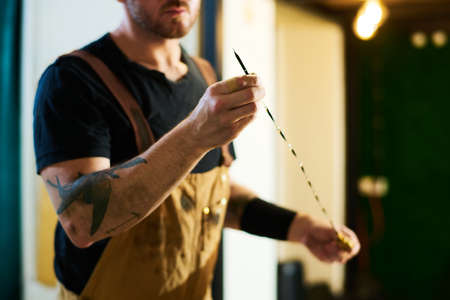 Young technician in apron holding sharp metallic wire while preparing work instrument for check up...