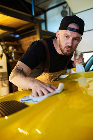 Young mechanic or technician of maintenance service cleaning cover of hood with detergent while...