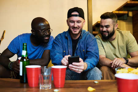 Young man with smartphone showing friends photos of his family or communicating in video chat while...