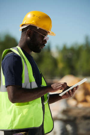 Young serious African American male engineer with tablet scrolling through online manual guide on territory of marble quarryの写真素材