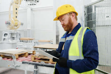 Young serious technician or foreman with tablet scrolling through technical data while searching for...