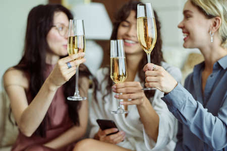 Three happy girls with champagne celebrating forthcoming wedding of one of them while holding flutes and making toast at hen partyの写真素材