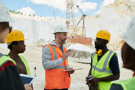 Confident middle aged foreman with document giving working instructions to African American...