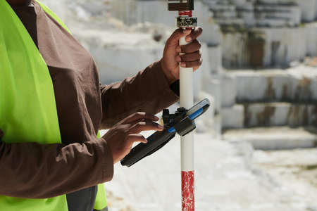 Hands of young black female worker of marble quarry scrolling through settings in smartphone while adjusting theodoliteの写真素材