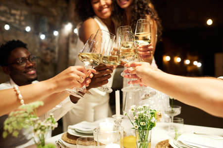 Hands of wedding guests and two intercultural brides clinking with flutes of champagne over festive...