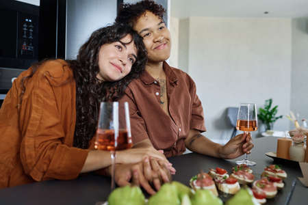 Young affectionate woman keeping head on shoulder of her smiling girlfriend with flute of champagne...