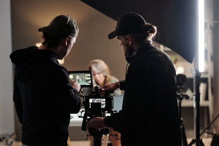 Back view of two young men standing in front of camer aand using steadicam while shooting new...