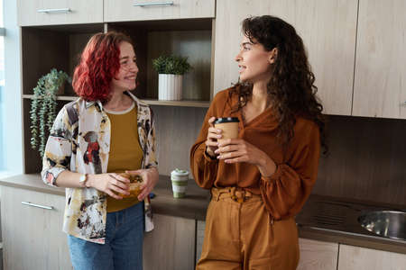 Two young elegant female employees in smart casualwear having coffee and lunch while standing in the...
