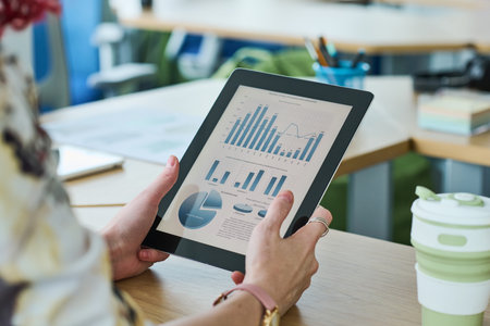 Hands of young female economist holding tablet with financial document on screen while sitting by...