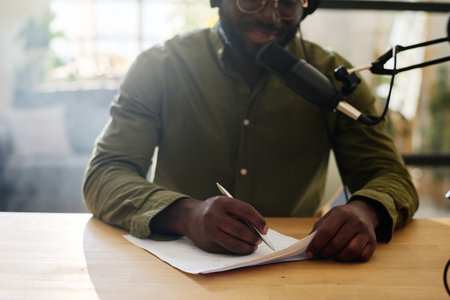Close-up of young black man pointing at paper with questions for interview and voicing one of them while talking in microphoneの写真素材