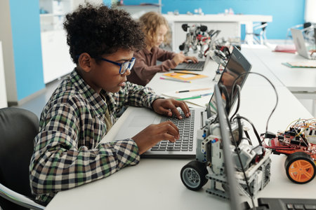 Side view of clever African American schoolboy sitting in front of laptop at lesson and searching for online information for projectの写真素材