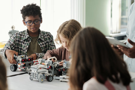 Cute intercultural schoolkids playing with toy robots which they created at lesson of robotics and their teacher with tablet standing behindの写真素材
