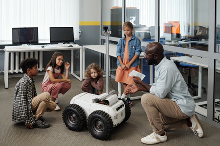 Young teacher of robotics with tablet making presentation of crawler to group of intercultural schoolkids while controling robot remotelyの写真素材